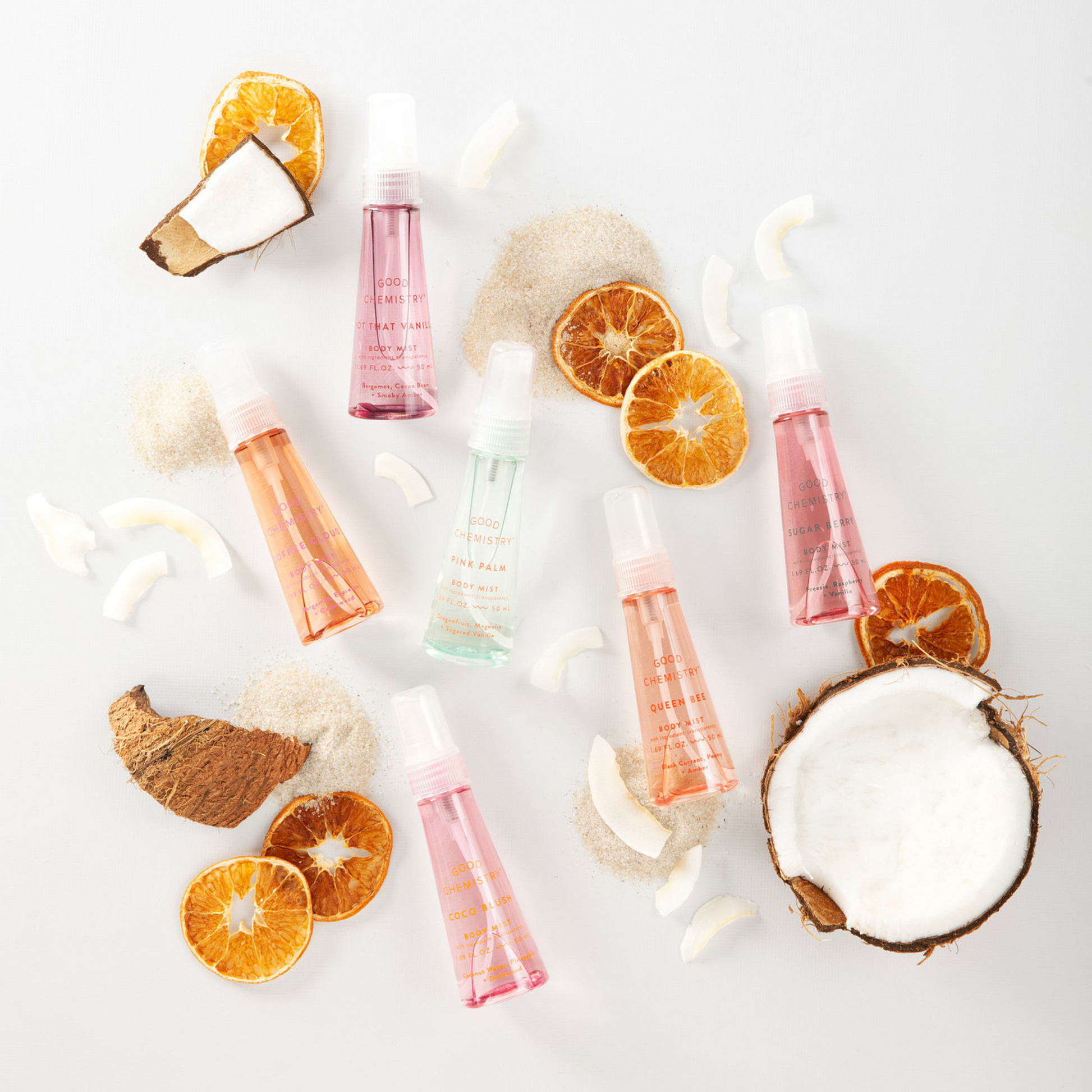 Good Chemistry assorted body mist bottles with orange slices and coconut on a white background