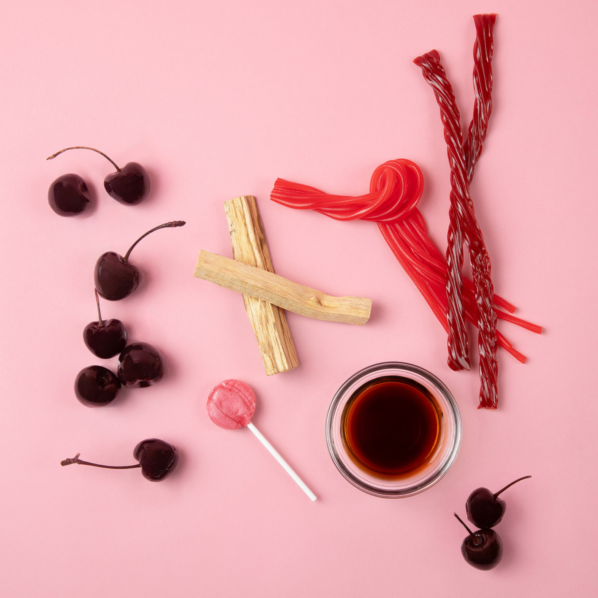 Good Chemistry Cherry Crush Ingredient Lifestyle Images featuring: candies including cherries, licorice, and a bowl of syrup on a pink background