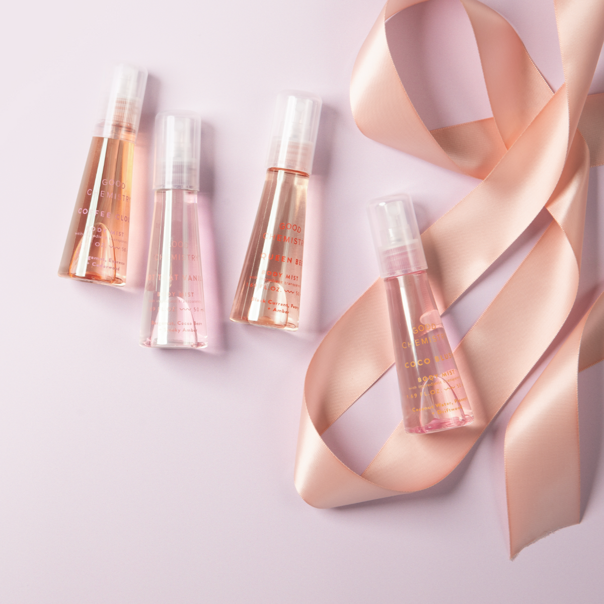Set of mini body gift set bottles out of gift packaging, including Coffee Cloud, Non That Vanilla, Queen Bee, and  Coco Blush with a pink ribbon on a light background