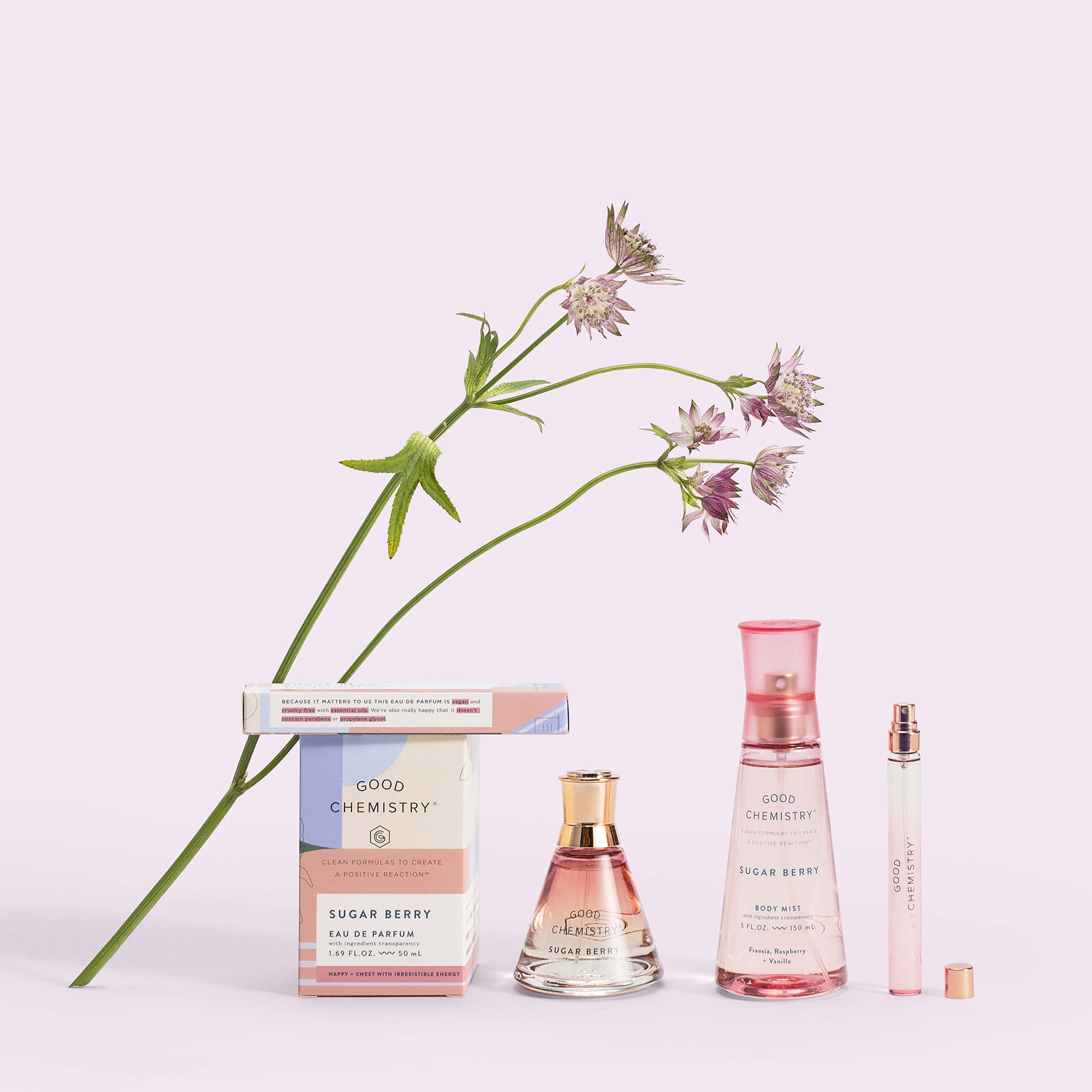 Two boxes labeled Good Chemistry Sugar Berry and three bottles (two big, one travel size) with a Freesia cutting against a pink background