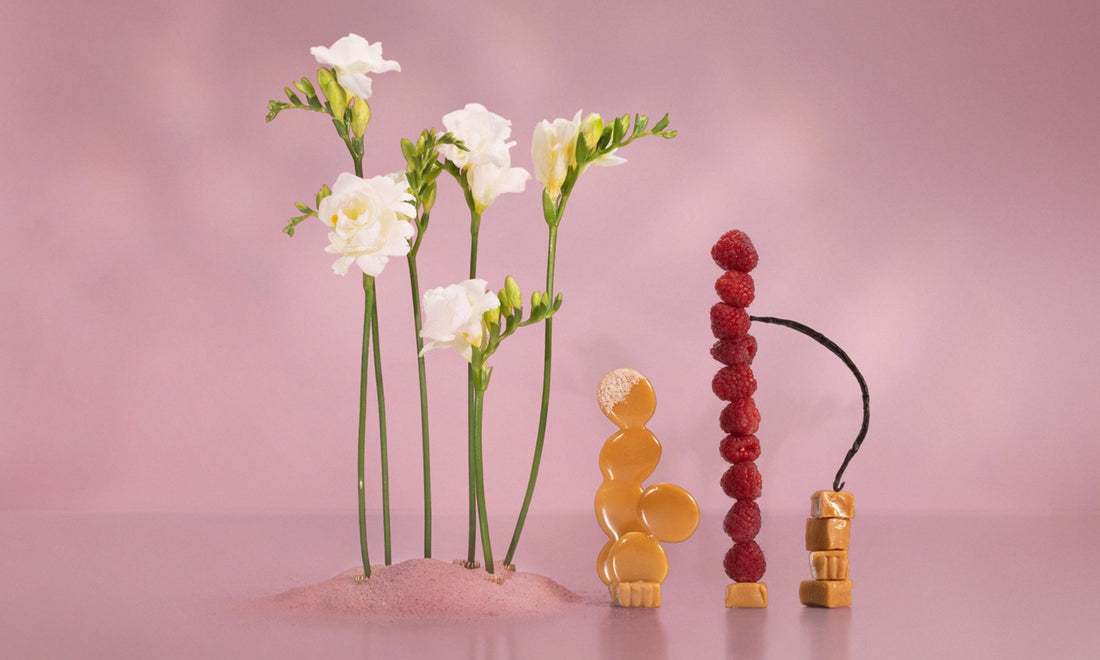Artistic arrangement of flowers and fruit on a pink background
