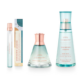 A set of three Unknown Legend fragrance bottles including a small travel spray, a medium-sized eau de parfum, and a larger body mist. The packaging is primarily light blue with floral and botanical illustrations, and the bottles contain liquids of varying concentrations for personal fragrance.
