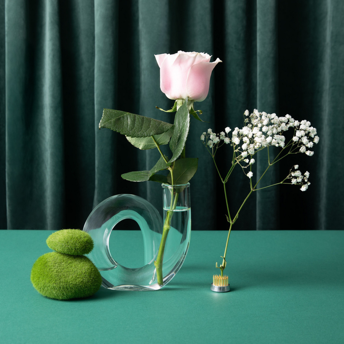 Clear glass vase with a pink rose and small white flowers on a green background