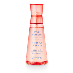 A clear pink spray bottle labeled 'GOOD CHEMISTRY CHEERFUL CHARMER BODY MIST' with text indicating fragrance notes of coconut milk, apple blossom, and vanilla.